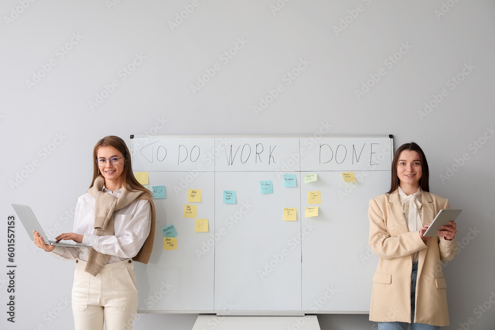 Young women with laptop and tablet computer near scrum task board in office