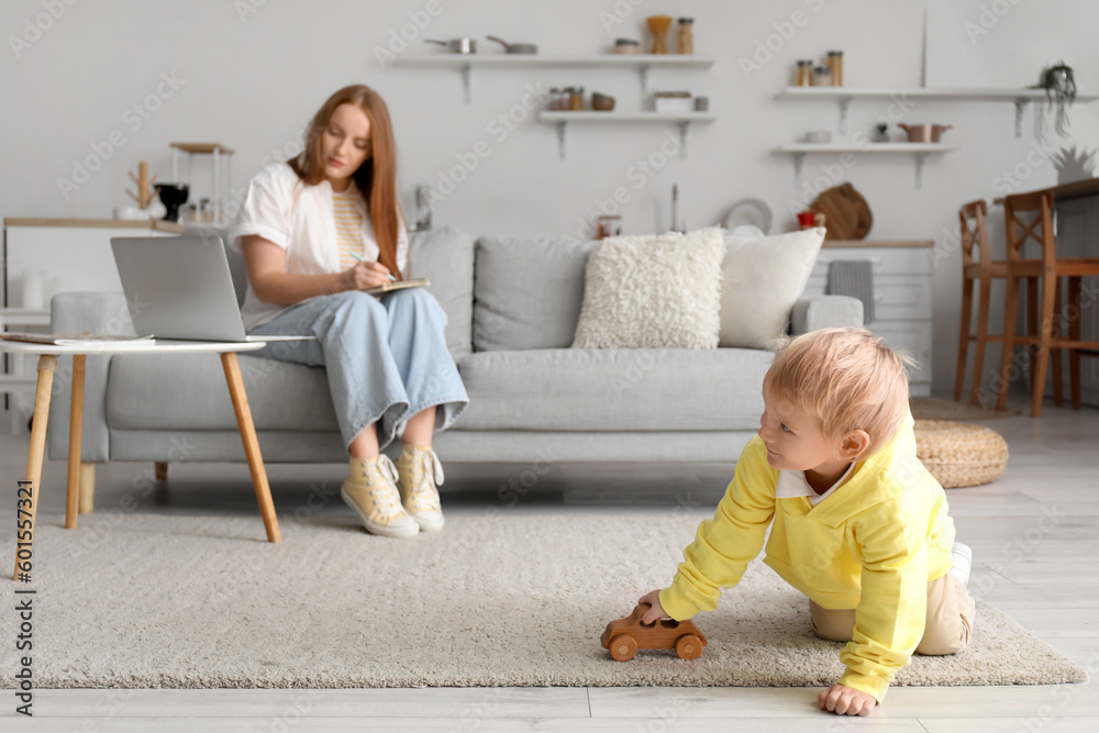 Little boy playing with wooden car and his working mother at home