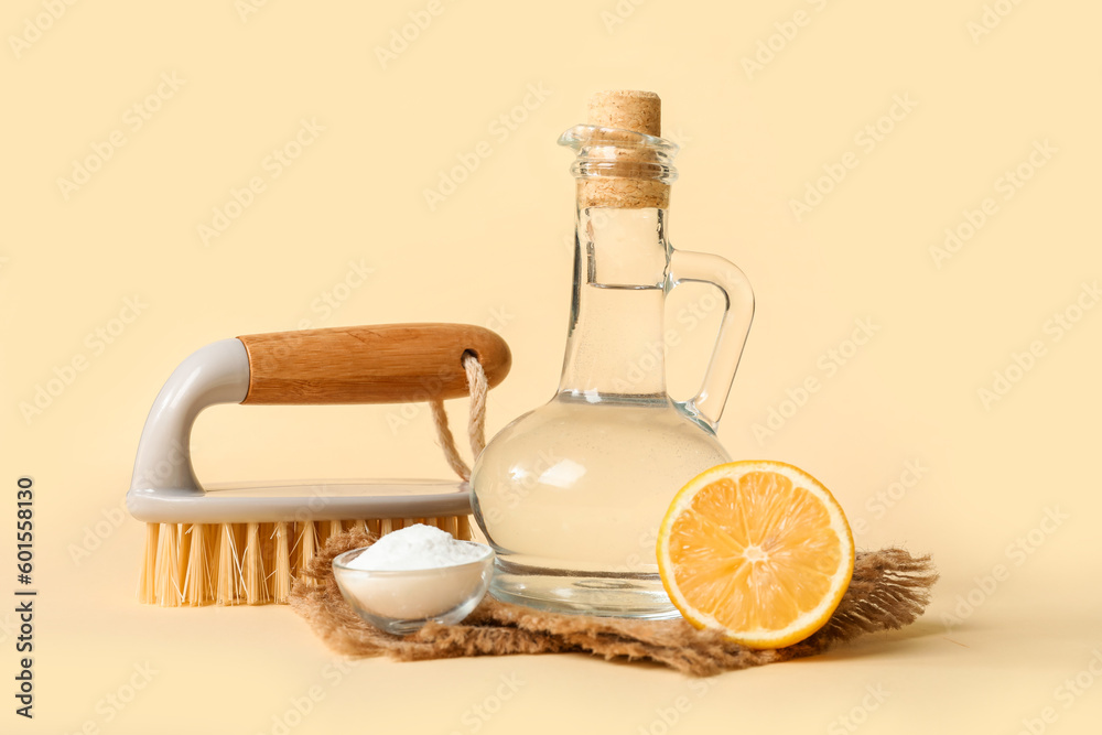 Jug of vinegar, baking soda, brush, lemon and napkin on color background