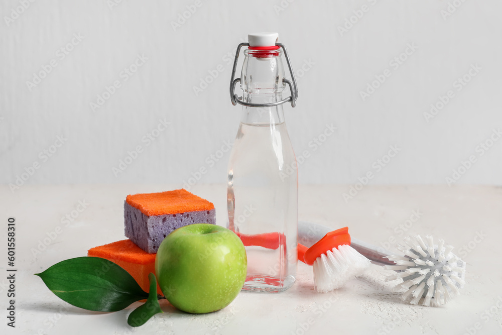 Bottle of vinegar, brushes, sponges and apple on light background