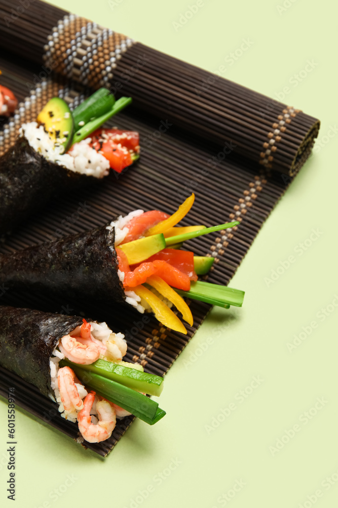 Bamboo mat with tasty sushi cones on color background, closeup