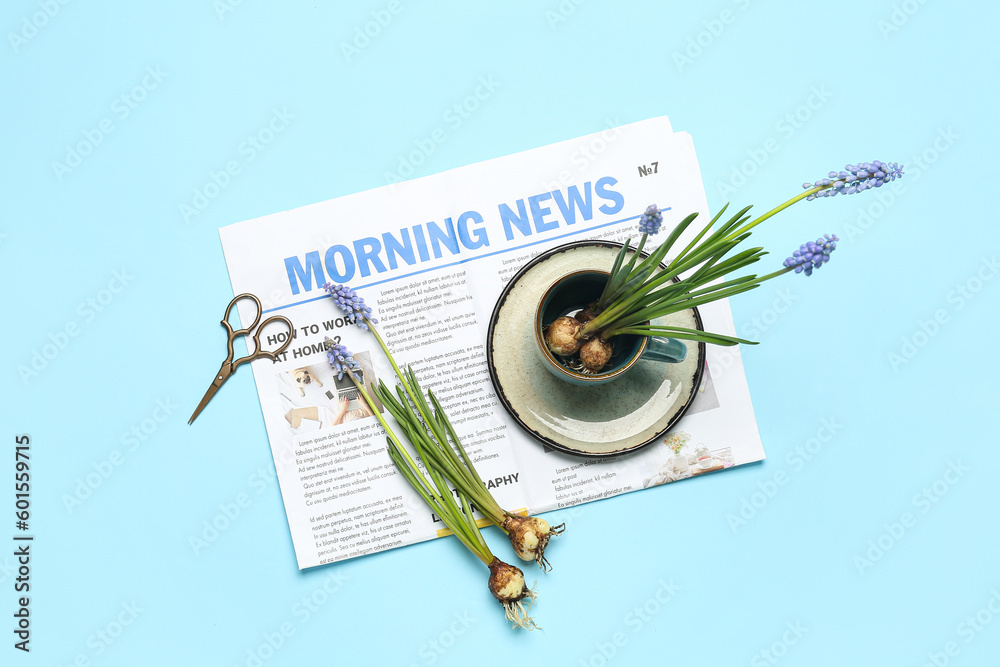 Composition with beautiful Muscari flowers, newspaper, cup and scissors on blue background