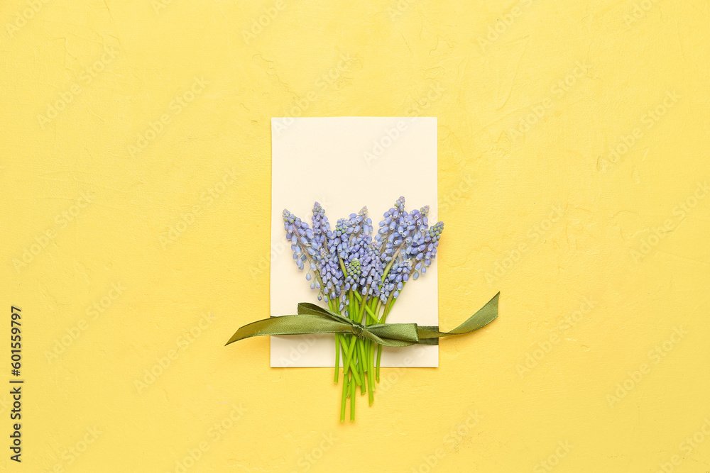 Blank greeting card with beautiful Muscari flowers and satin ribbon on yellow background