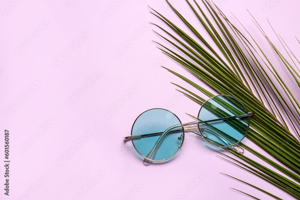 Round sunglasses with palm leaf on lilac background