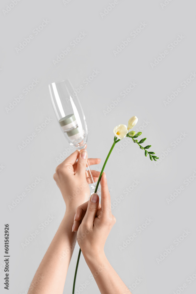 Hands holding glass with cream and flowers on light background