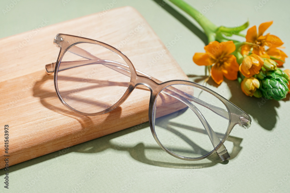 Notebook, flower and eyeglasses on pale green background