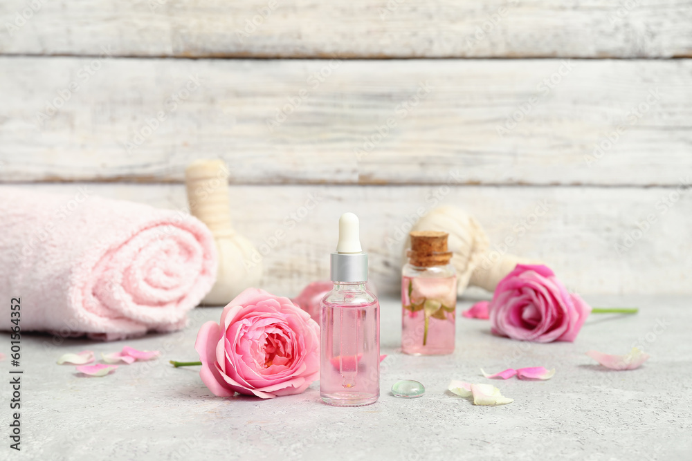 Bottles of cosmetic oil with rose extract and flowers on white table