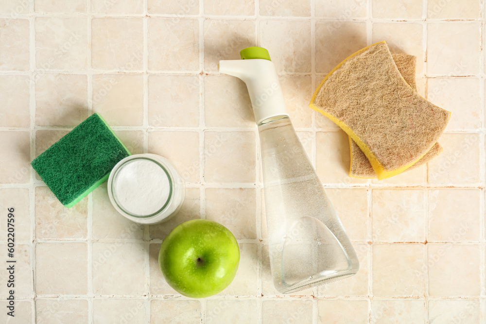 Bottle of vinegar, baking soda, sponges and apple on light tile background