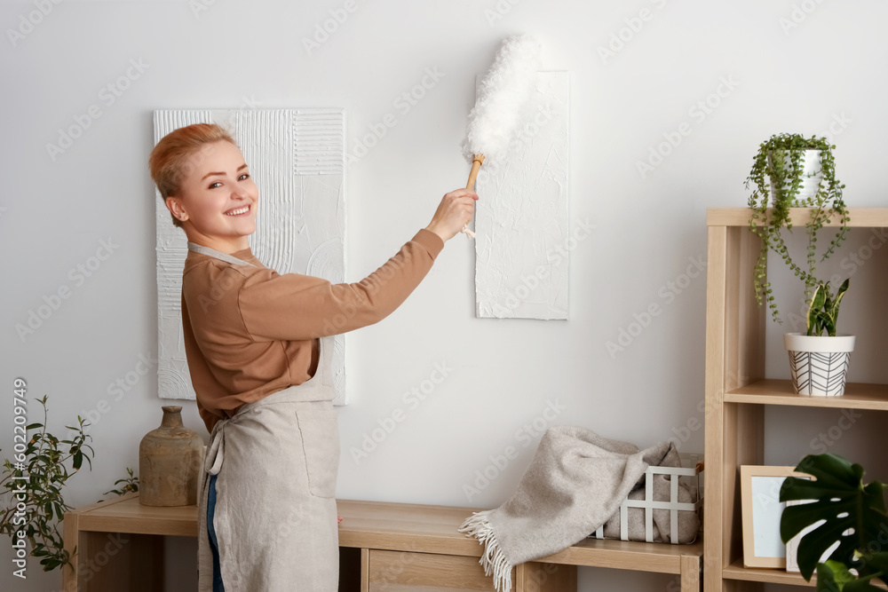 Young woman cleaning painting with pp-duster at home