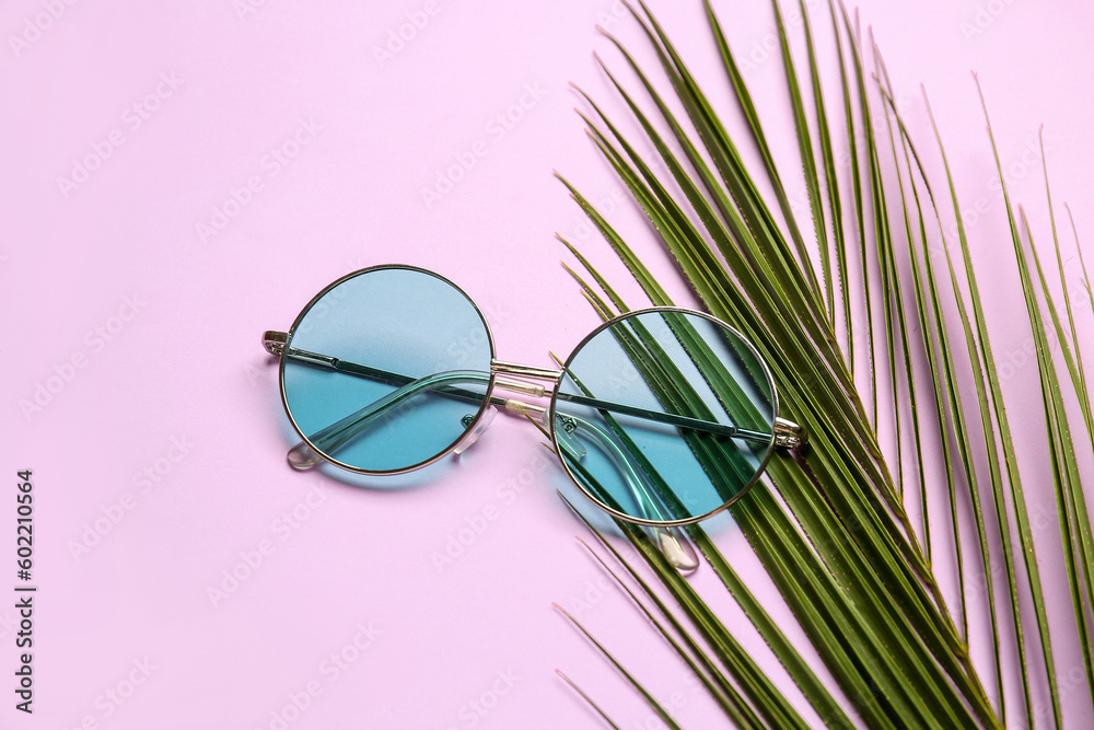 Round sunglasses with palm leaf on lilac background