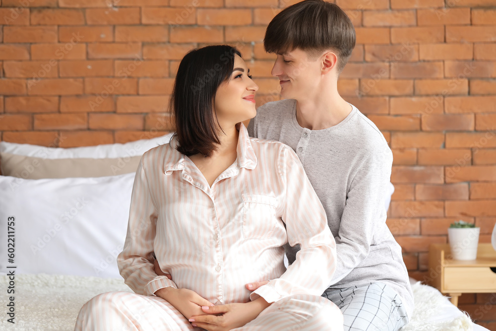 Young pregnant couple sitting in bedroom