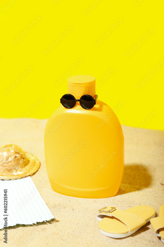 Creative composition with bottle of sunscreen cream in sunglasses and beach accessories on sand