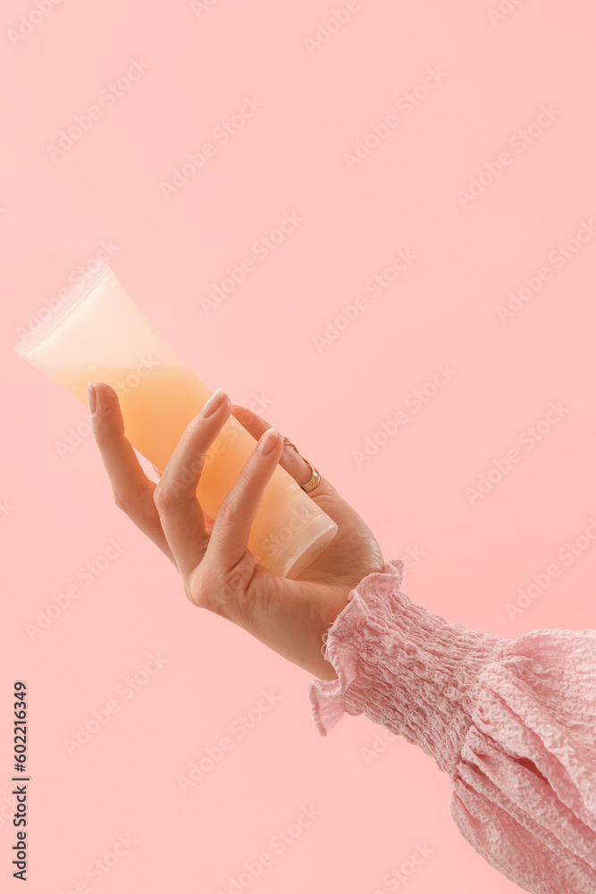 Hand holding cosmetic product on pink background