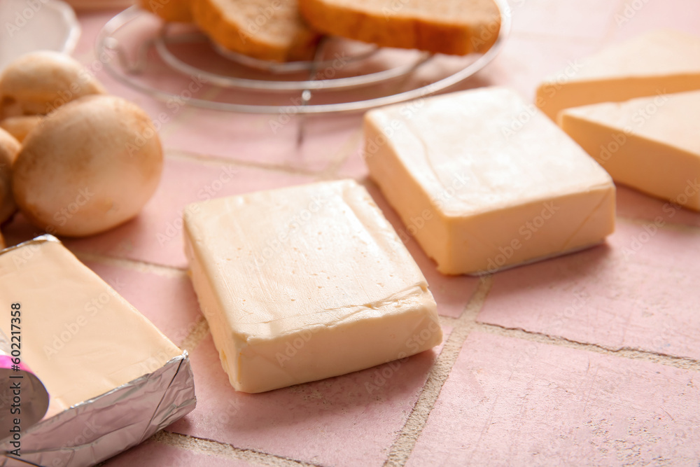 Processed cheese, bread and vegetables on pink tile background