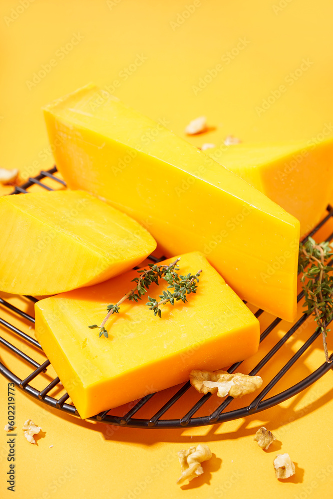 Stand with tasty cheddar cheese, thyme and nuts on orange background, closeup