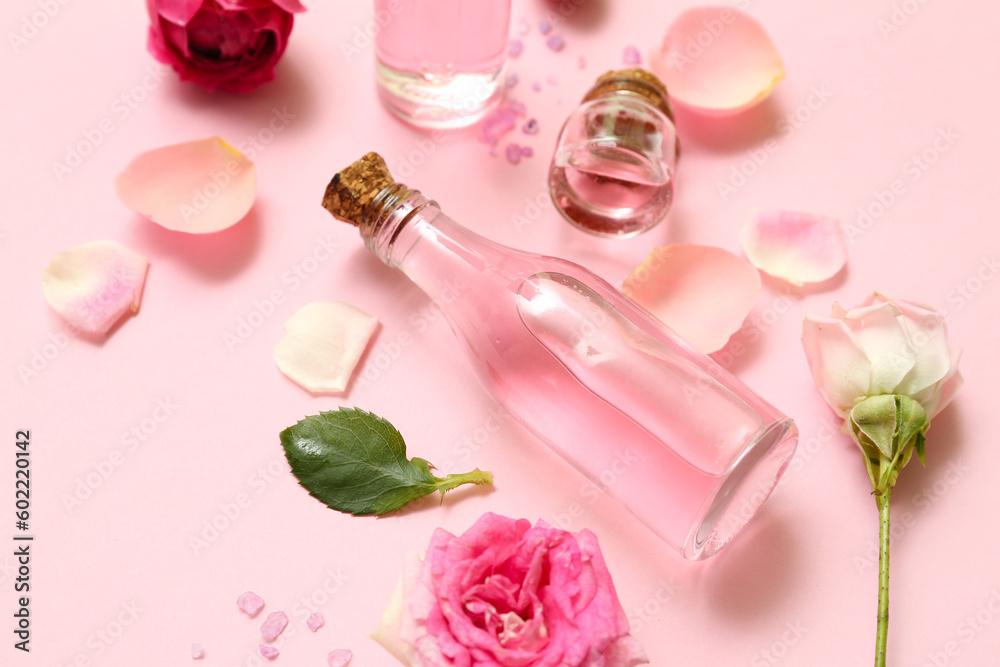 Bottles of cosmetic oil with rose extract and flowers on pink background