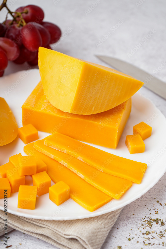 Plate with tasty cheddar cheese on light background