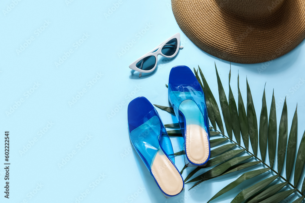 Pair of high heeled sandals with sunglasses and hat on blue background