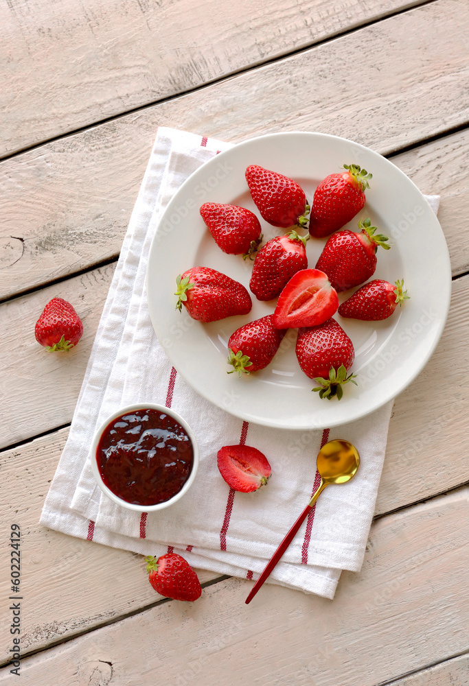 Plate with fresh strawberries and jam on white wooden background