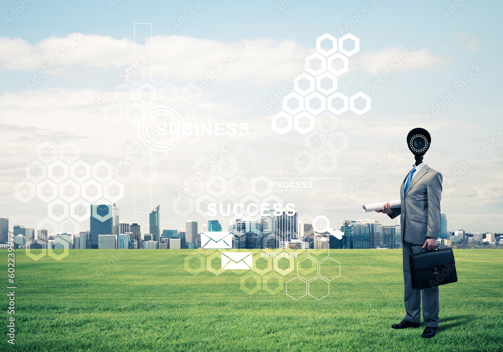 Camera headed man standing on green grass against modern cityscape