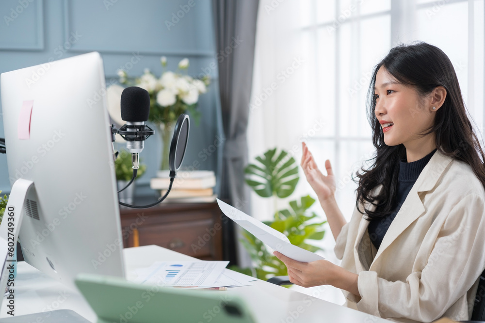 Young Asian woman having online meeting or recording podcast on computer with headphones and microph