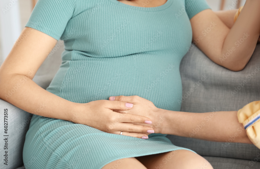 Young pregnant couple sitting on sofa at home, closeup