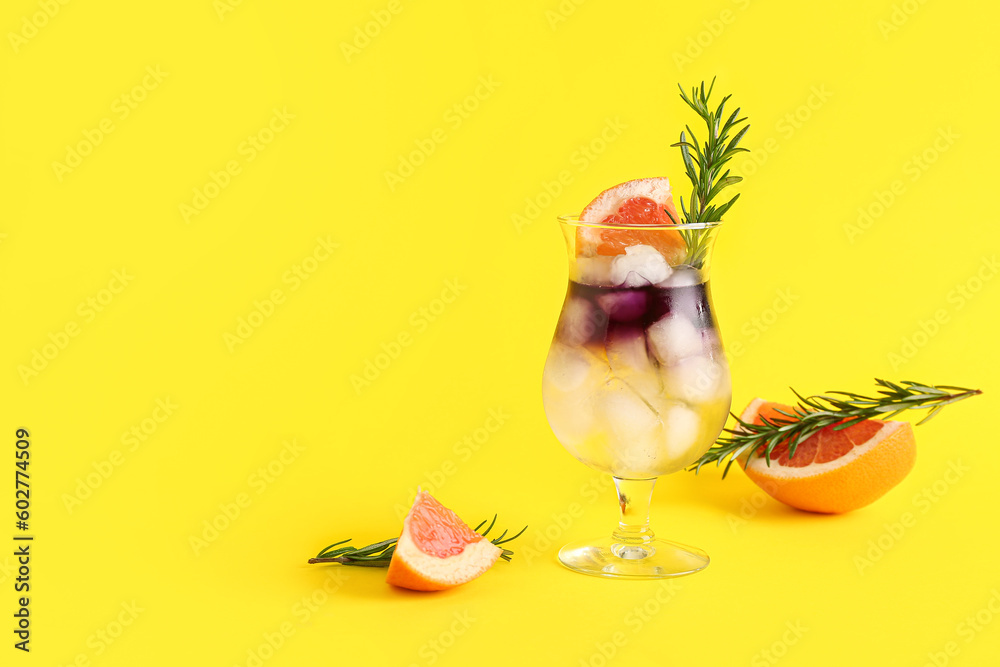 Glass of purple gin and tonic with grapefruit and rosemary on yellow background