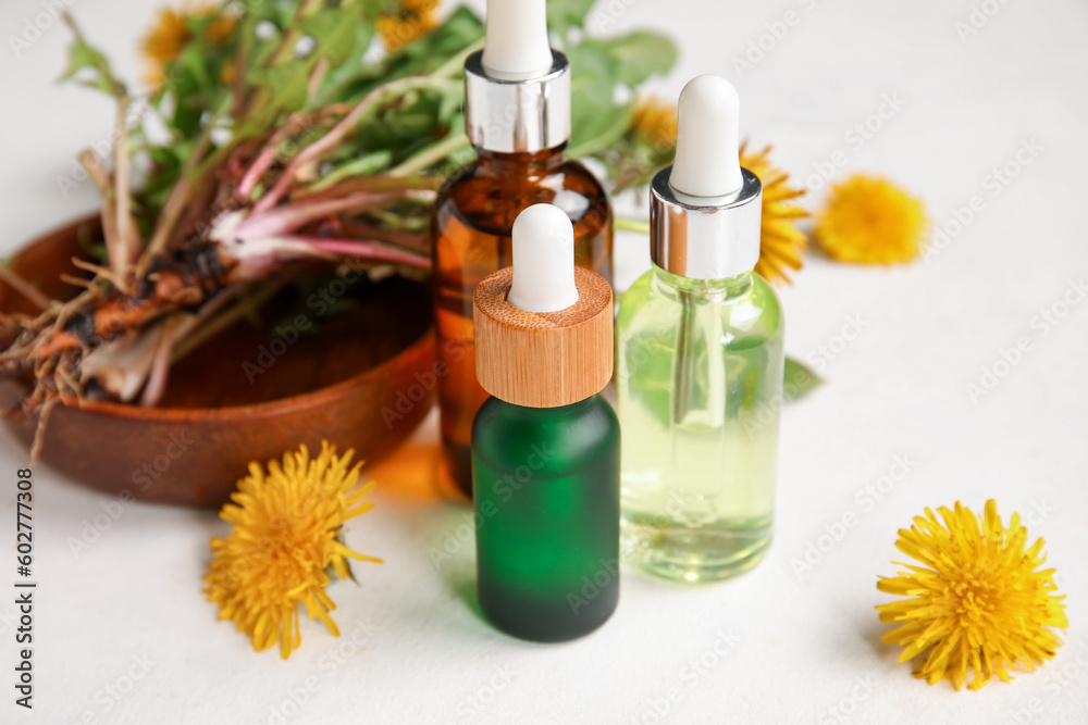 Bottles with cosmetic oil and plate of dandelion flowers on white background