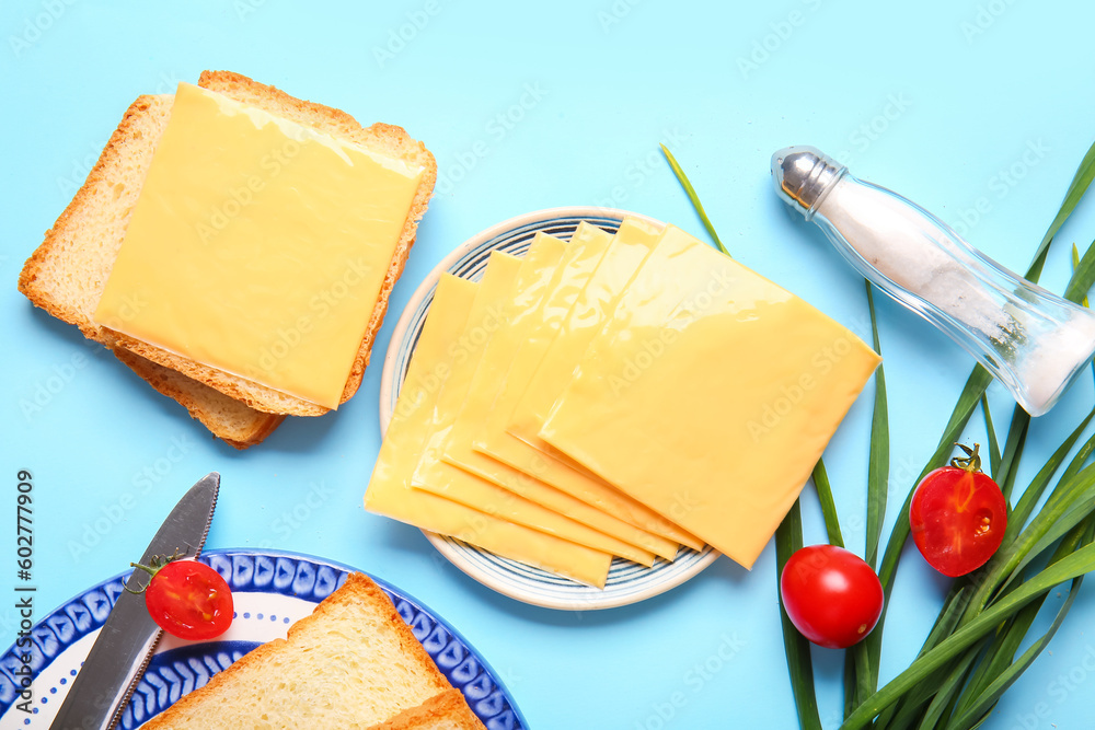 Plates of tasty processed cheese with bread and vegetables on blue background