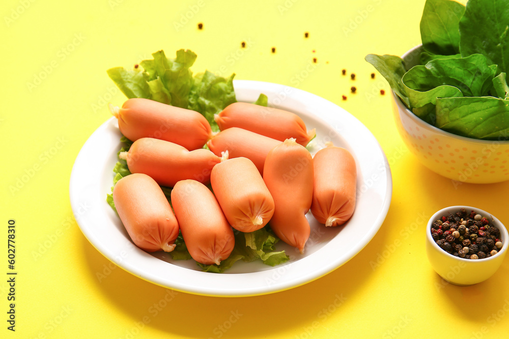 Plate of tasty boiled sausages and bowl with spinach on yellow background