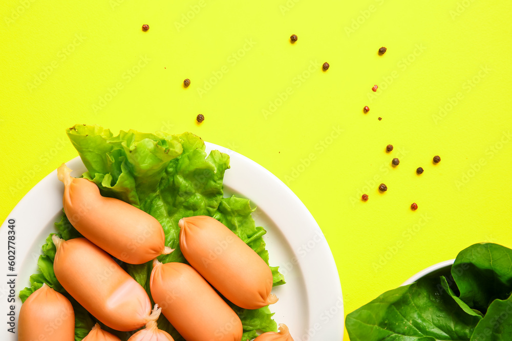 Plate of tasty boiled sausages and lettuce on yellow background