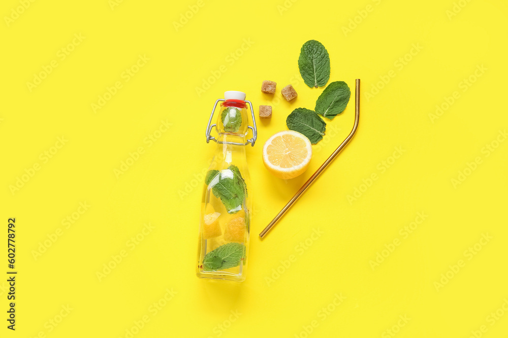 Glass bottle of lemonade with lemons, mint and ginger on yellow background