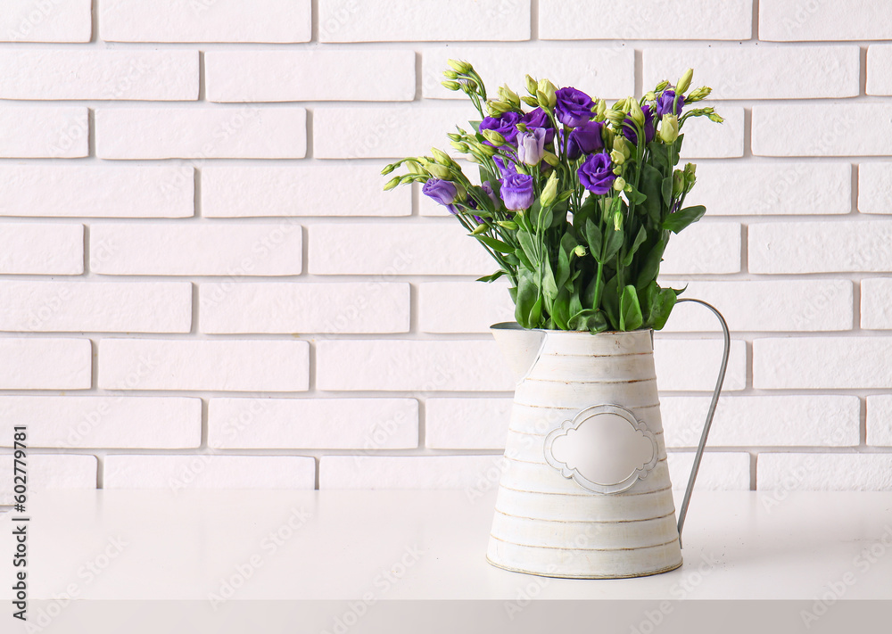 Jug with eustoma flowers on table near white brick wall