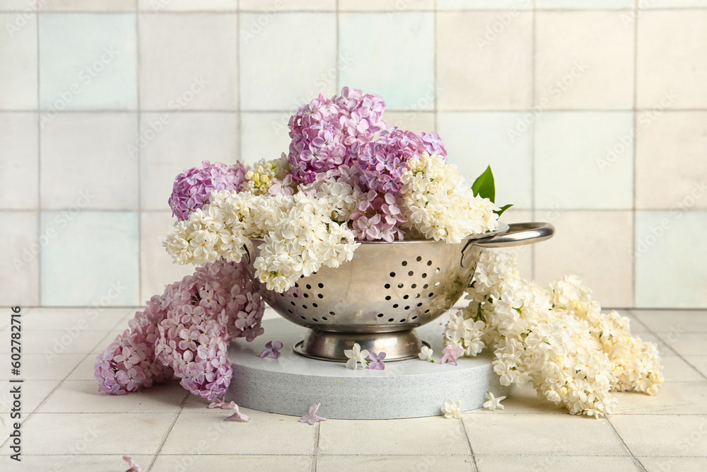 Colander with Beautiful fragrant lilac flowers near white tile