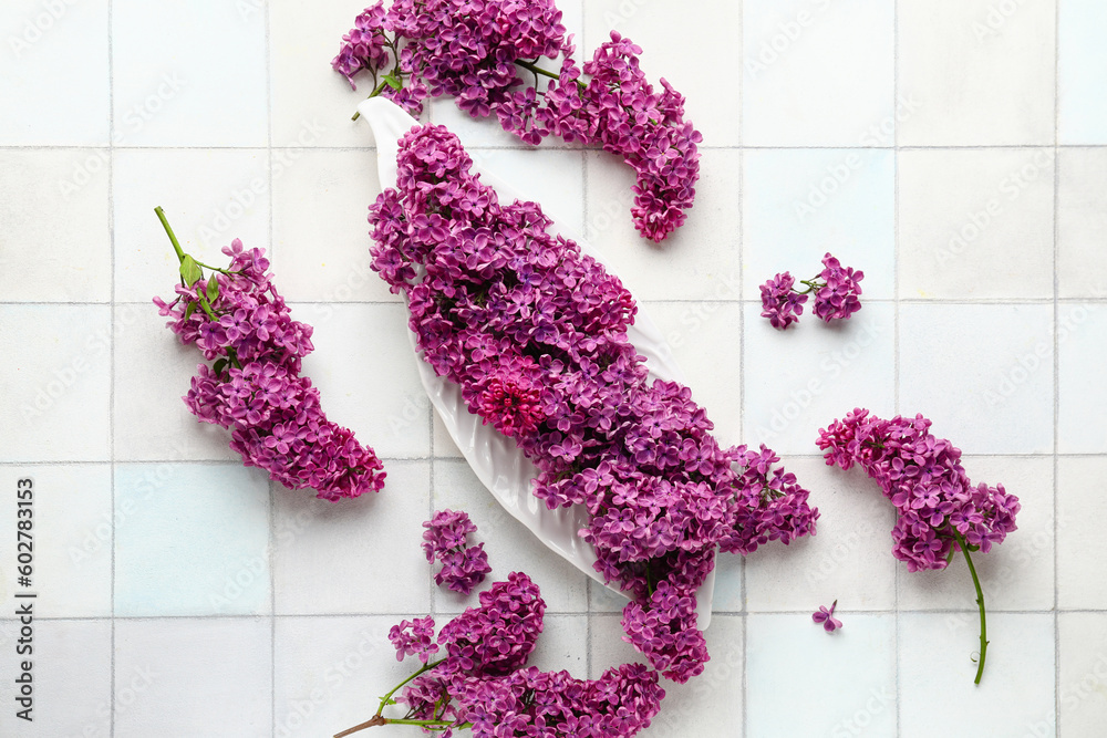 Plate of beautiful fragrant lilac flowers on white tile