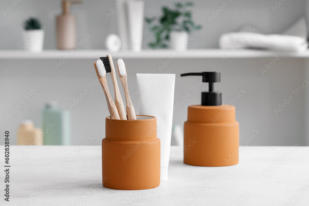 Holder of bamboo toothbrushes, soap and paste on white table in room