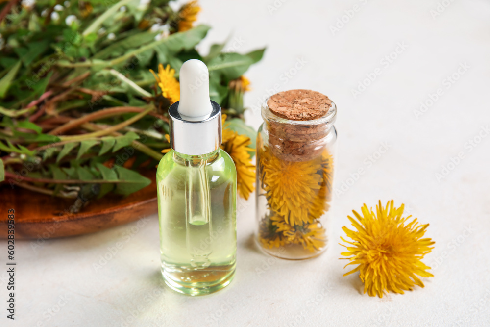 Bottles with cosmetic oil and plate of dandelion flowers on white background