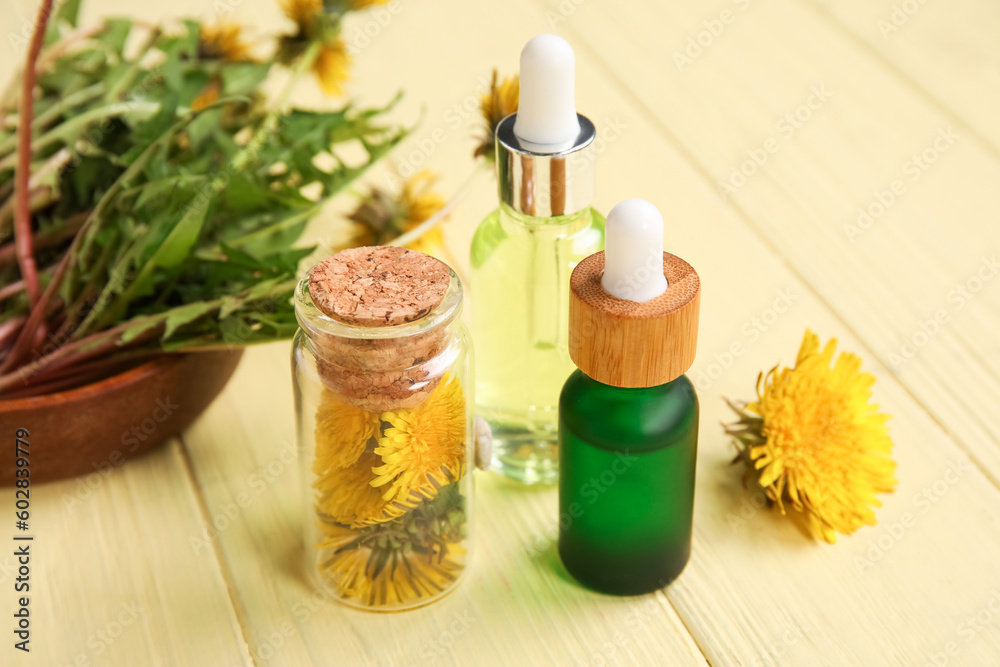 Bottles with cosmetic oil and bowl of dandelion flowers on yellow wooden background