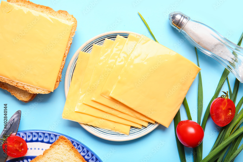 Plates of tasty processed cheese with bread and vegetables on blue background