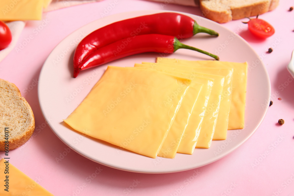 Plate of tasty processed cheese with bread and chilli on pink background