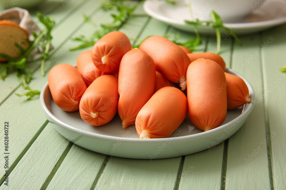 Plate of tasty boiled sausages with arugula on green wooden background