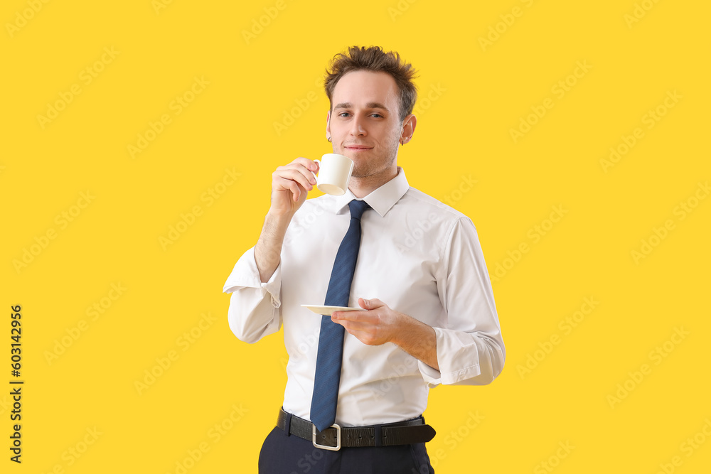 Young businessman with cup of coffee on yellow background