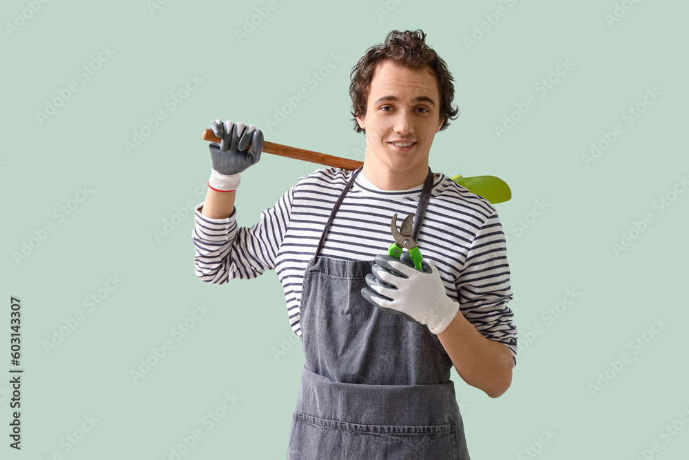 Male gardener with secateurs and shovel on green background