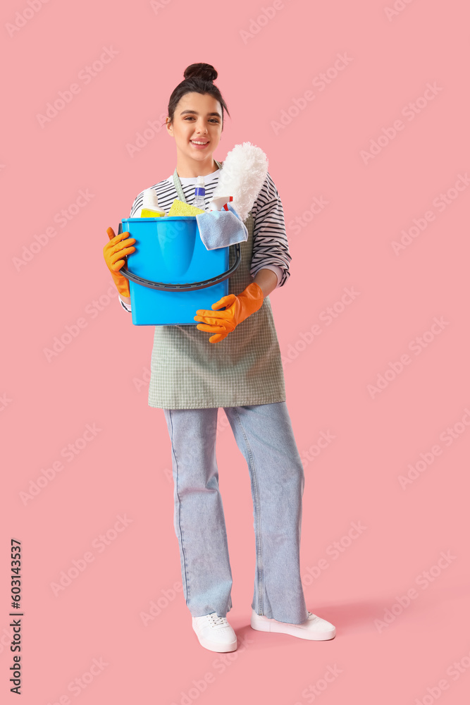 Young woman with cleaning supplies  on pink background