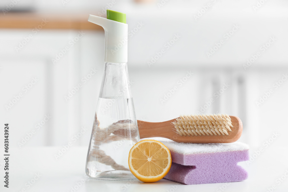 Bottle of vinegar, sponge, brush and lemon on table