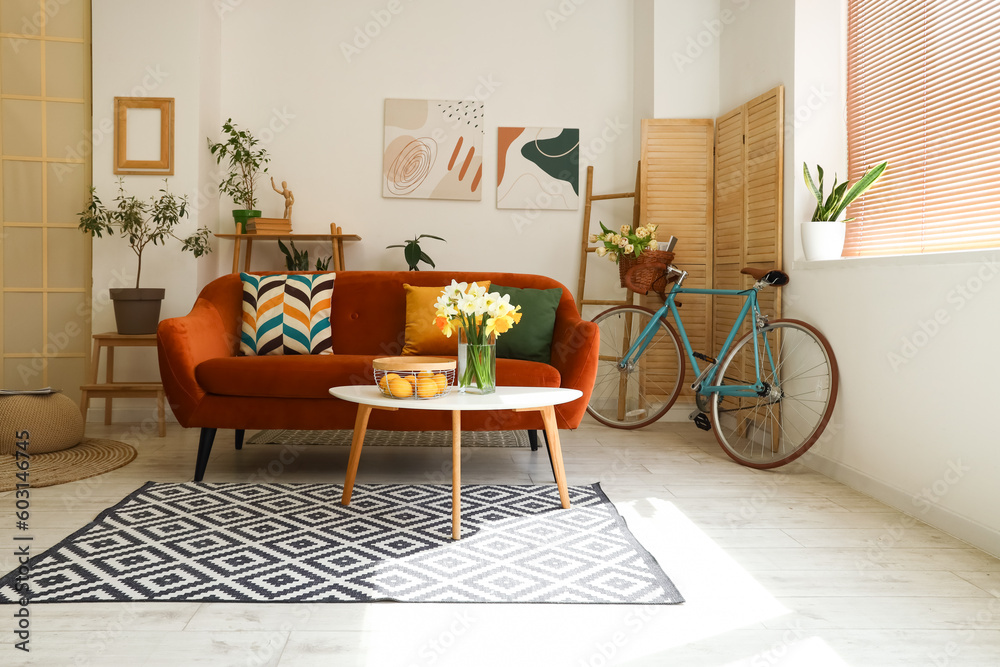 Interior of light living room with cozy brown sofa and narcissus flowers on coffee table