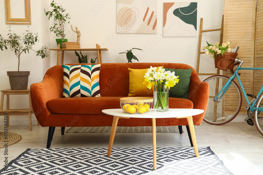 Interior of light living room with cozy brown sofa and narcissus flowers on coffee table