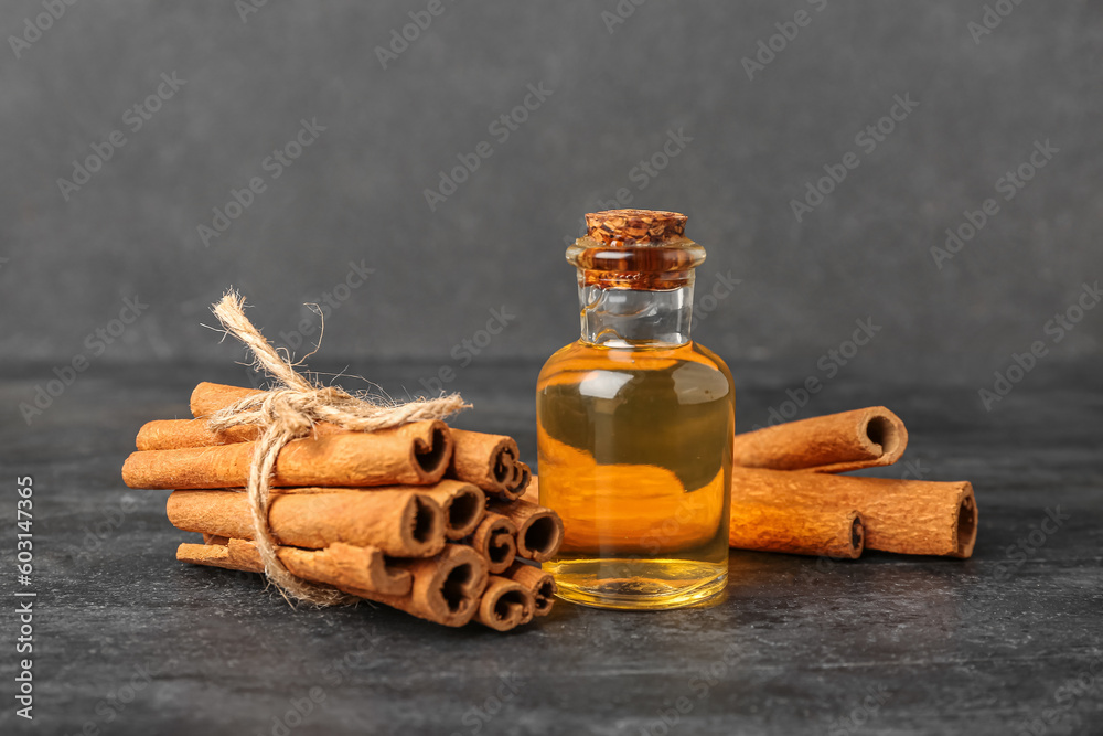 Bottle of essential oil and cinnamon sticks on dark background