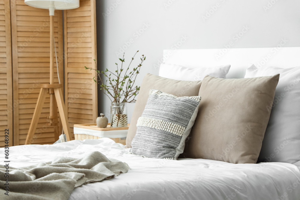 Cozy bed with many pillows and blooming tree branches on bedside table