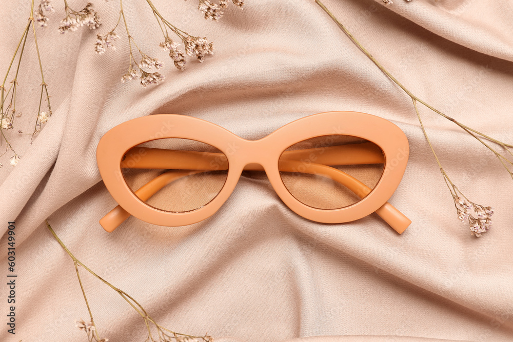 Stylish sunglasses with flowers on beige fabric background